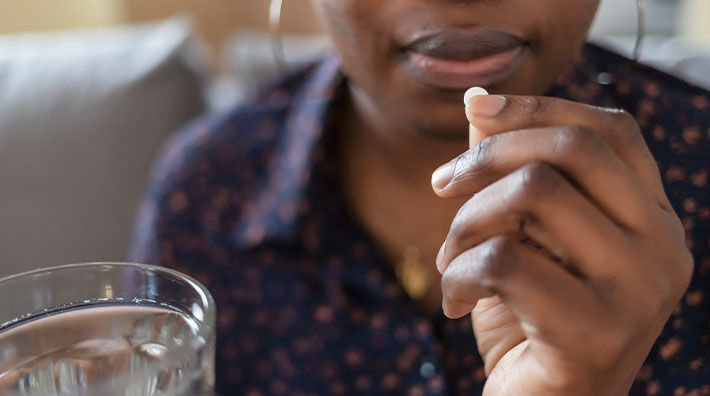 A person holds an aspirin in their hand close to their mouth