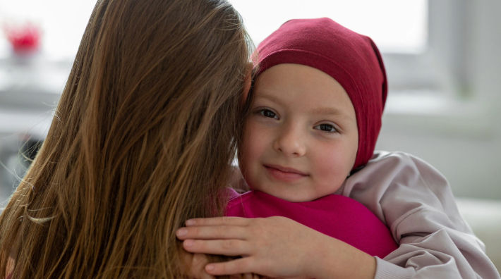 A child wearing a maroon head covering hugs a person with long brown hair.