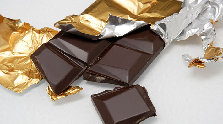 Squares of a dark chocolate bar wrapped in gold foil on a white background