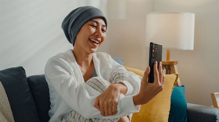 A woman wearing a knit cap and a white cardigan uses her smartphone while sitting on a couch