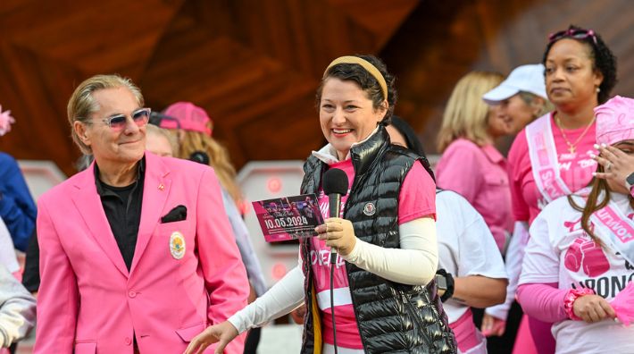 Charlotte de Brabandt speaks at a breast cancer awareness event wearing a pink shirt, black vest and gold headband