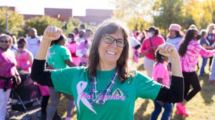 Woman with green shirt and brown hair smiles while flexing bicep muscles at a cancer awareness event