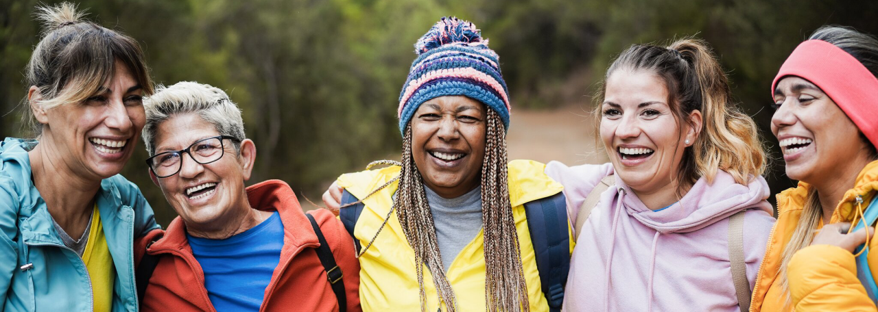 Group of diverse middle-aged women laughing and enjoying a hike outdoors, wearing colorful casual hiking gear